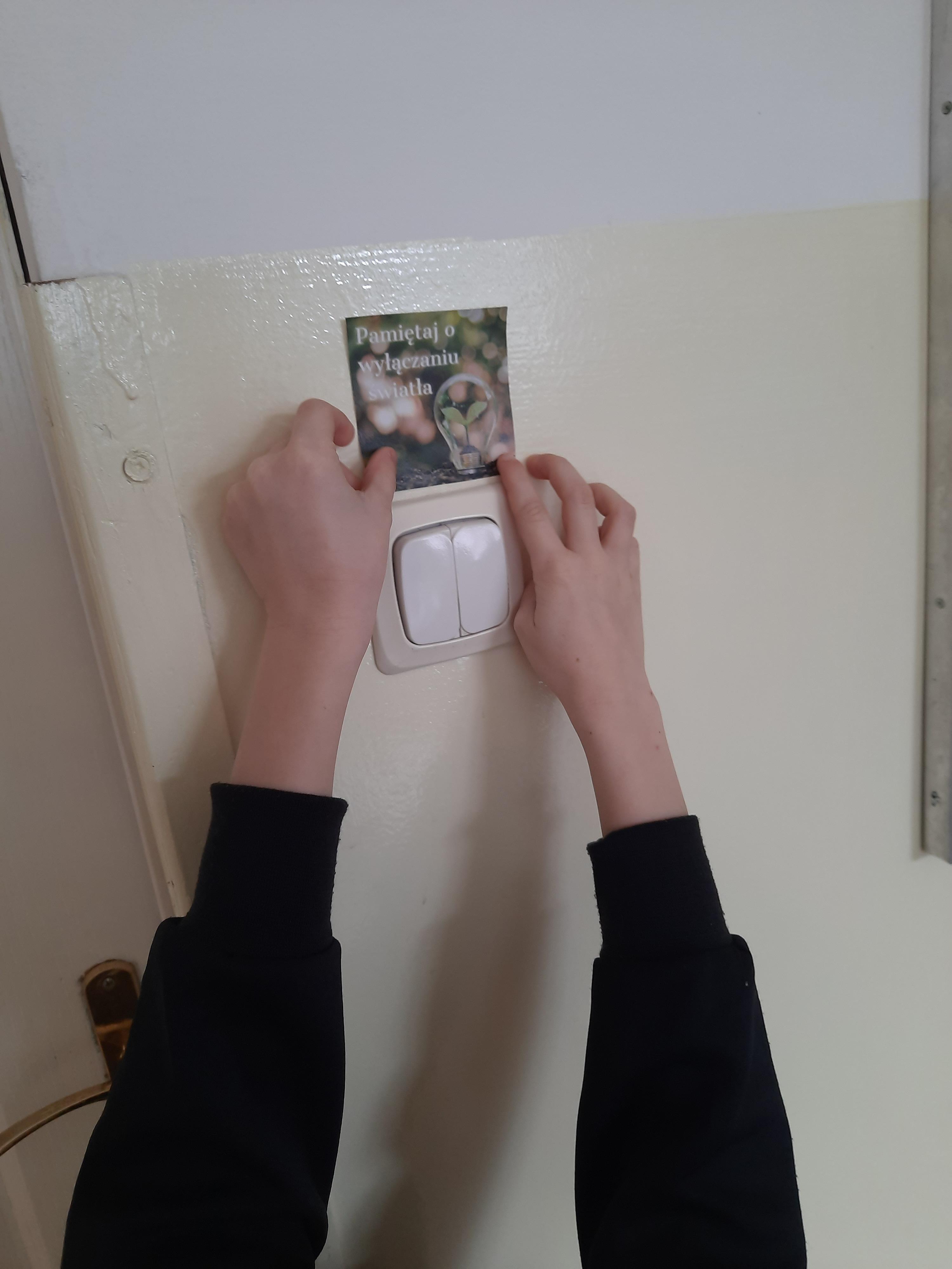 Pierwszoklasista_przykleja_nad_włącznikiem_światła_naklejkę_przypominającą_o_oszczędzaniu_energii-